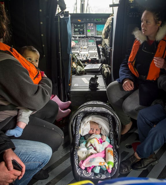 small baby in car seat sits between adults on a helicopter floor
