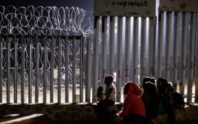 Migrants from Guatemala, part of the Central American migrant caravan, are seen near the US-Mexico border fence in Mexico on December 9, 2018. -
