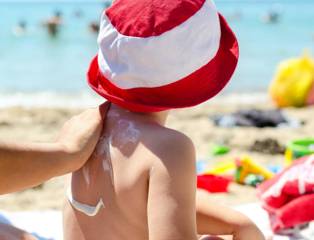 Child on the beach putting sunscreen.