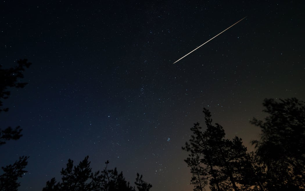 Night scene with starry sky and meteorite trail over forest. Long exposure shoot