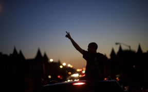 Young people in cars drive towards a phlanx of Baltimore riot police honking their horns and raising their hands with peace signs the night after citywide riots.