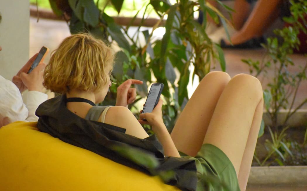 A young person slouches in a yellow bean bag, scrolling on their phone.