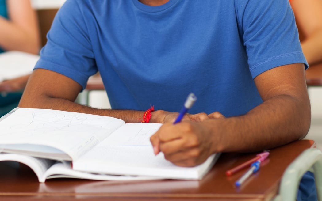 A young man in a classroom, writing, in a file photo to illustrate foreign students.