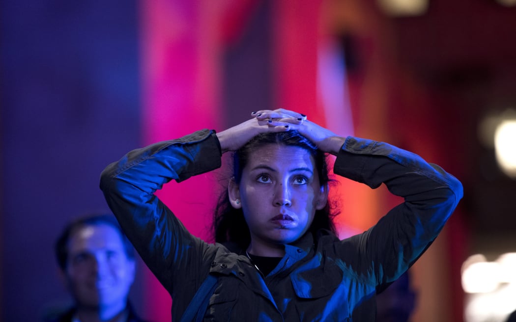A woman reacts watching the midterm election primary results on a screen at the Rockefeller Center in New York.