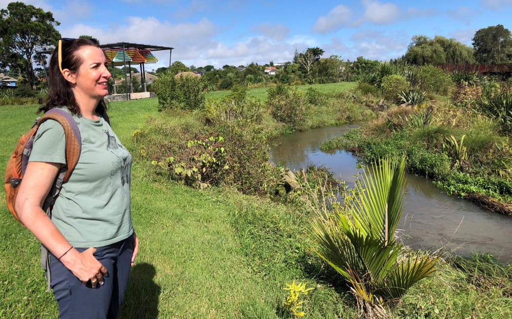 Auckland councillor Julie Fairey is standing in a park on a sunny day, next to a stream.
