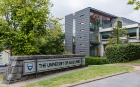 Auckland, New Zealand - March 1, 2017: Sign and logo of University of Auckland set near modern dark gray offices in green park like environment. Gray sky.