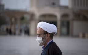 A Iranian cleric wearing a face mask walks near a shrine in the holy city of Qom, March 2020..