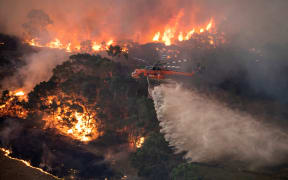 A handout photo taken and received on December 31, 2019 from the State Government of Victoria shows a helicopter fighting a bushfire near Bairnsdale in Victoria's East Gippsland region.