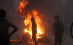 Iraqi demonstrators stand behind a tyre fire during a demonstration against state corruption, failing public services, and unemployment, in the Iraqi capital Baghdad on October 5, 2019. - )