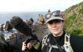 Michelle Roper on bird recording field work on an offshore island. She is holding a microphone.