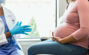 An unrecognizable female doctor wears protective mask and gloves as she prepares to examine an unrecognizable pregnant woman.
