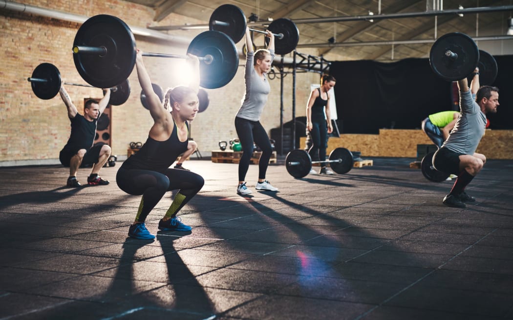 Group of young muscular adult male and females lifting large barbells in cross-fit class with thick mats and brick walls