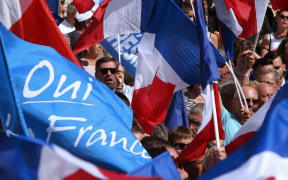French far-right party Front National (FN)'s supporters hold French National flags and FN's flags as they listen to their president near a banner which translates as "Marie saves France" on September 3, 2016 during a FN