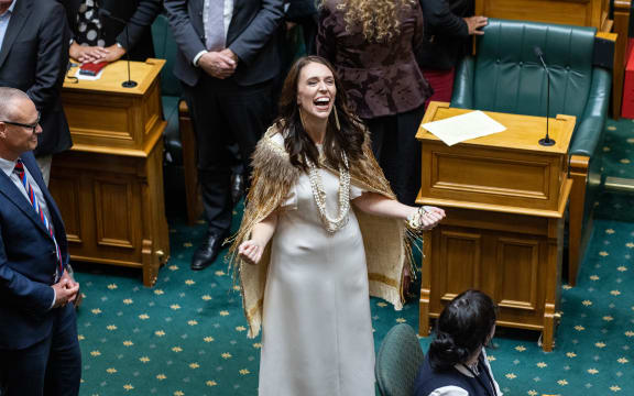 Jacinda Ardern interacts with her daughter from the floor of the debating chamber after her valedictory speech at Parliament. Her arms are wide and she looks like someone recently freed.