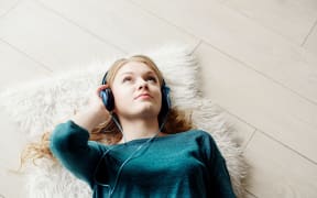 Beautiful blond woman listening to music through headphones. Lying on a wooden floor.