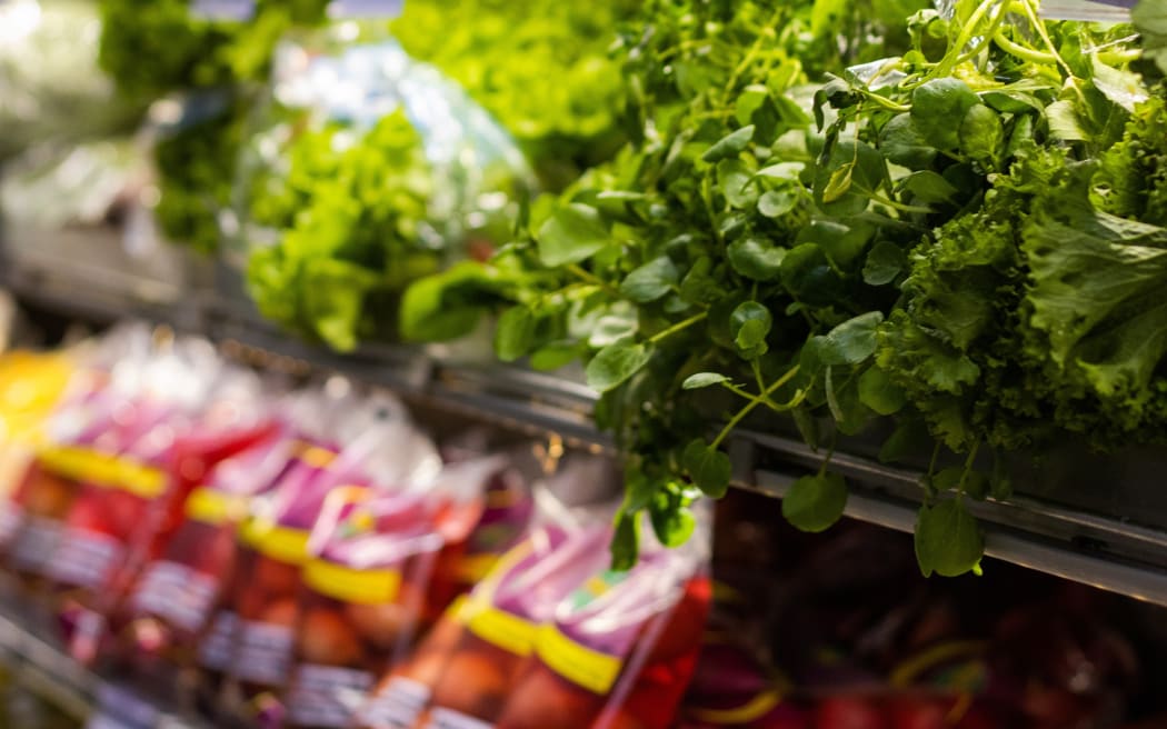 Produce including lettuces and other vegetables stacked in supermarket shelves.