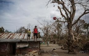 (Foreground) a child and an elderly man stand on the roof of a dwelling damaged Cyclone Pam, on Ifira Island, just off the coast of the main island of Efate.