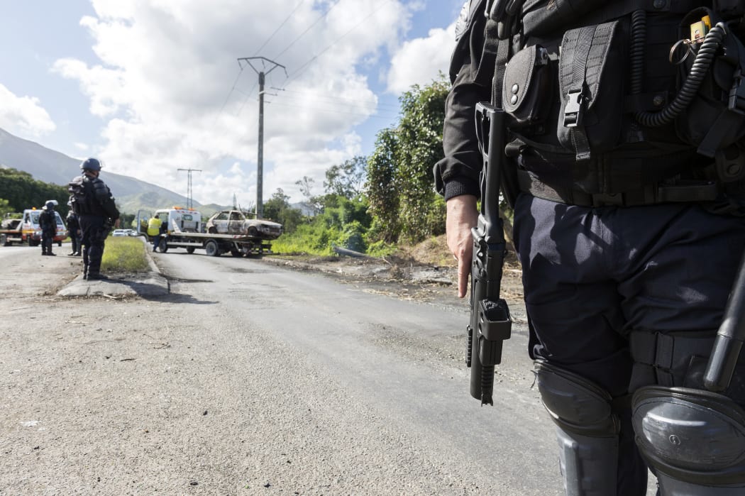 French police officers stand guard on a road in Mont-Dore, a suburb of Noumea, in New Caledonia, on May 28, 2014, while a tow lifts the wreckage of a burned car. Angry residents from the Saint Louis tribal group burned cars creating roadblocks on May 24, 2014