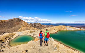 New Zealand popular tourist hiking hike in Tongariro Alpine Crossing National Park. Tramping trampers couple hikers walking on famous destination in NZ.
