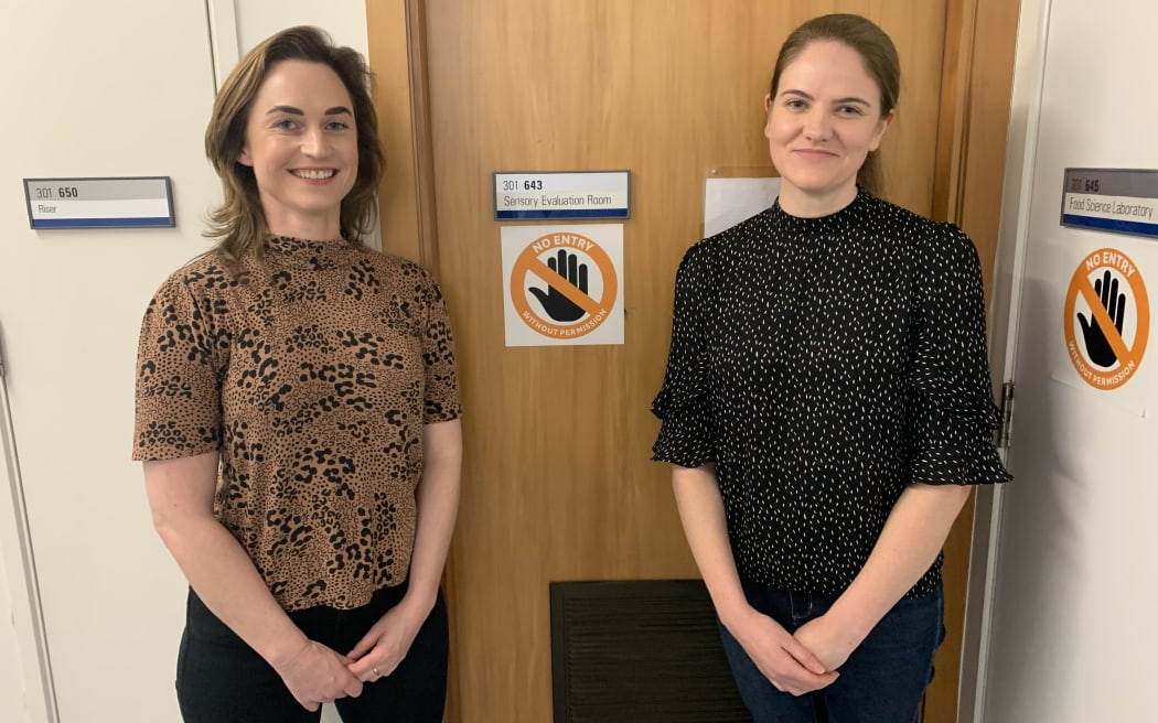 Dr Rebecca Jelley and Dr Danaé Larsen stand in front of a closed wooden door leading to a sensory laboratory. Both women are smiling.