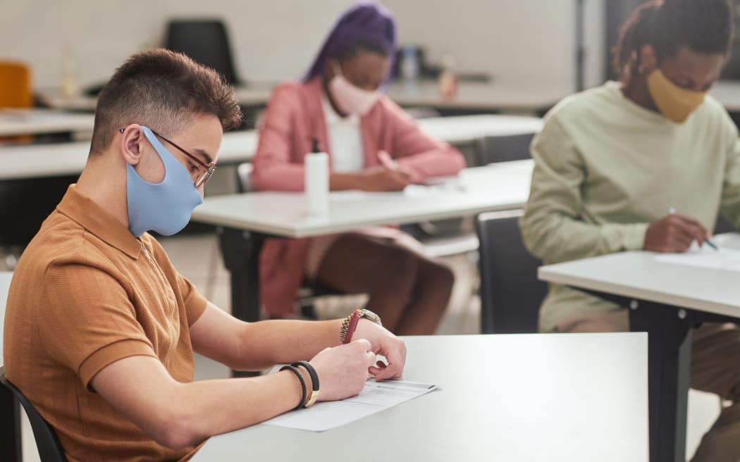 Side view portrait of young man wearing mask while taking test or exam in school with diverse group of people, copy space