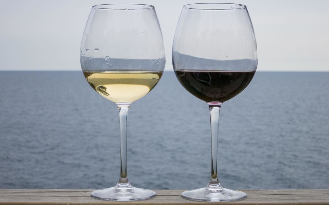 Glasses of wine - one white, one red - against a backdrop of a lake or the sea.