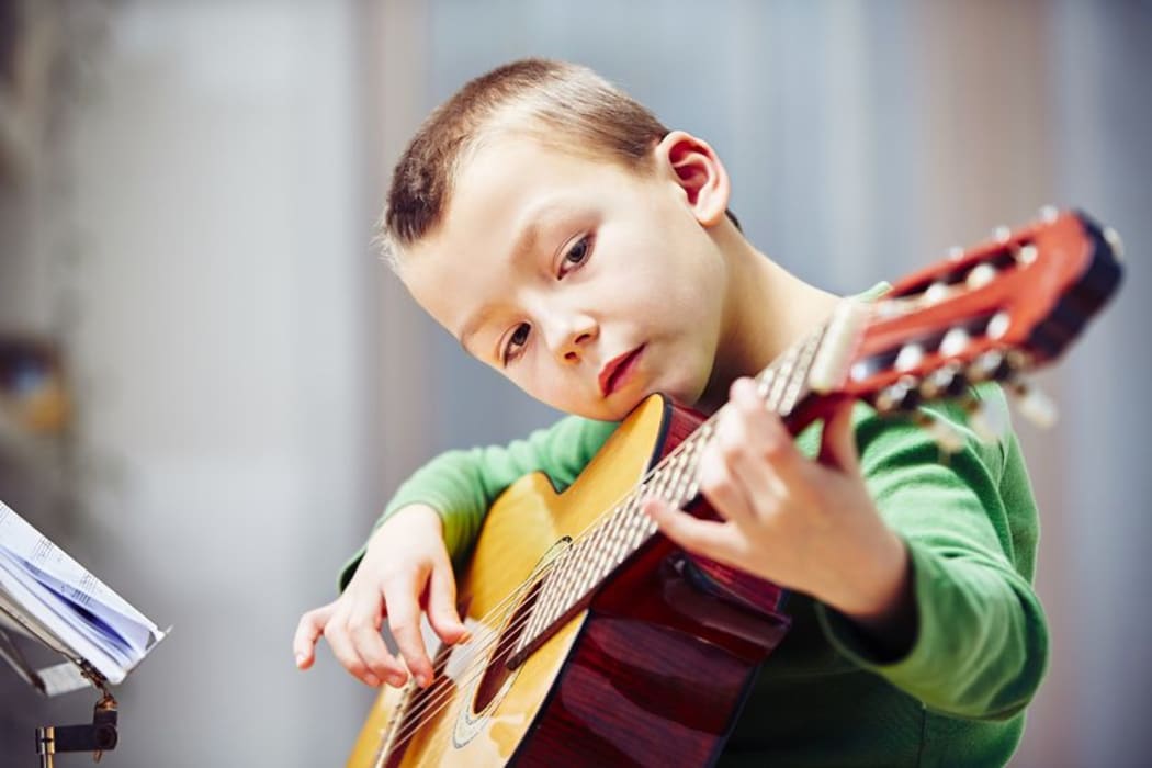 A photo of a little boy playing the guitar at home