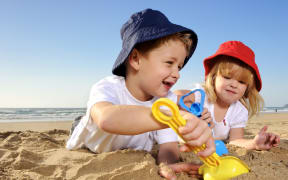 Two children wearing hats play with spades on a sunny day at the beach.