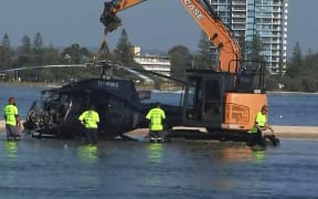 In this handout photo taken and released on January 3, 2023 airport workers prepare to remove a crashed helicopter that collided with another helicopter in Gold Coast on January 2, killing four.