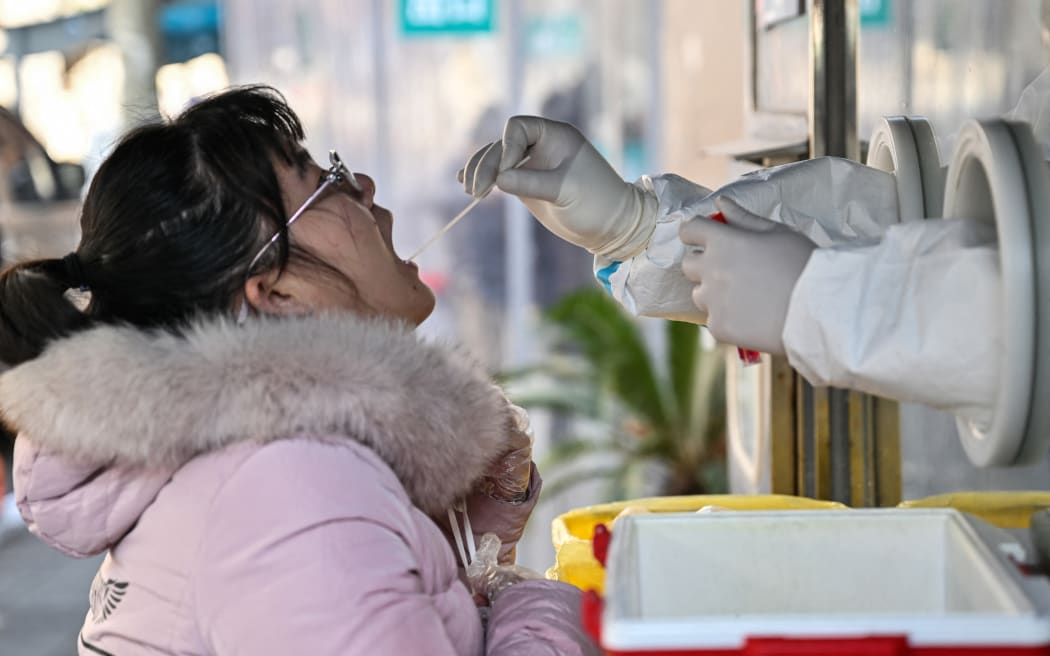 Un trabajador de la salud toma una muestra de hisopo de una mujer para detectar el coronavirus Covid-19 en el distrito de Jing'an, Shanghái, el 22 de diciembre de 2022. (Foto de Hector RETAMAL/AFP)