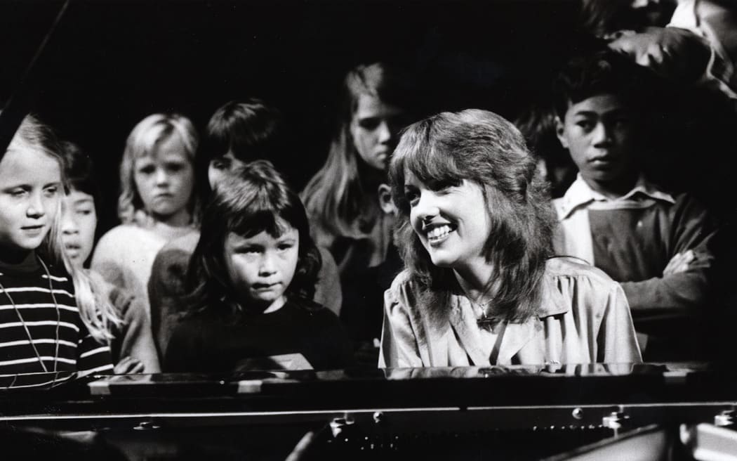 Sharon O'Neill (1978) plays piano surrounded by children.