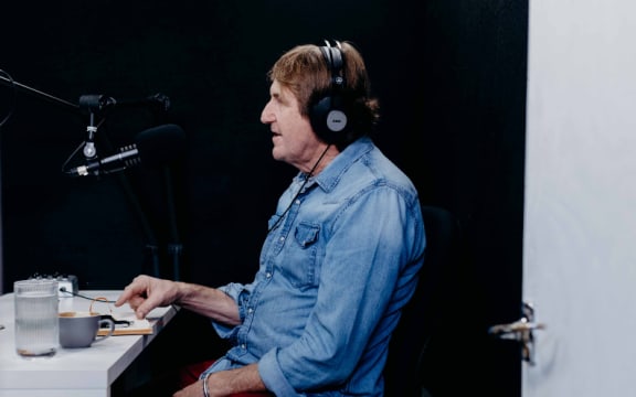 Journalist Cameron Bennett wearing headphones in a small broadcasting studio