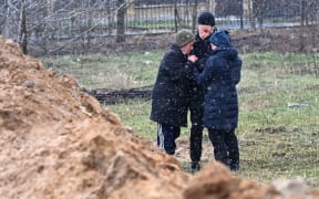 People gather close to a mass grave in the city of Bucha, just northwest of the Ukrainian capital Kyiv on 3 April, 2022.