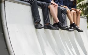 A group of school children in uniform sit on the edge of a skateboard bowl