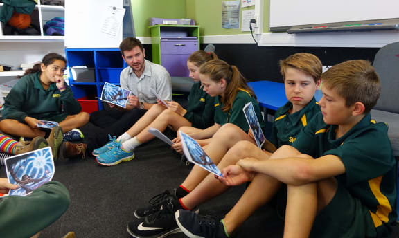 Children sit on the floor with teacher looking at books