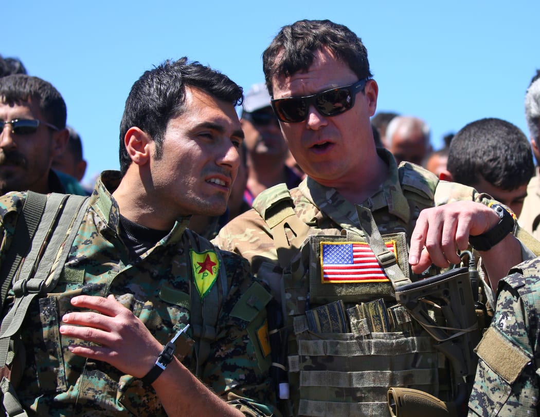 a US officer, from the US-led coalition, speaking with a fighter from the Kurdish People's Protection Units (YPG) at the site of Turkish airstrikes near northeastern Syrian Kurdish town of Derik.