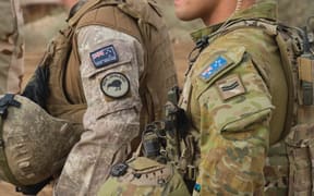 Close up of New Zealand and Australian soldiers side by side in uniform with their country flag on their sleeves.