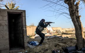 A fighter with the Syrian Democratic Forces (SDF) takes aim with his Kalashnikov assault rifle after seeing a man walking towards his position in the town of Baghouz