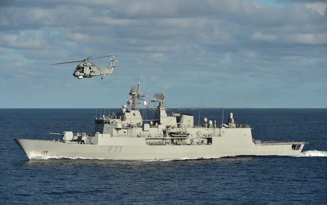 The HMNZS Te Kaha out at sea with a helicopter flying above
