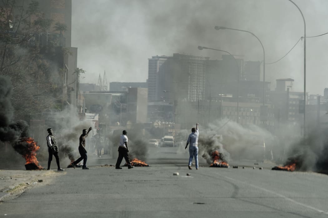 Protesters gesture towards police officers (not seen) as they burn tyres in Jeppestown, Johannesburg, on 11 July, 2021.
