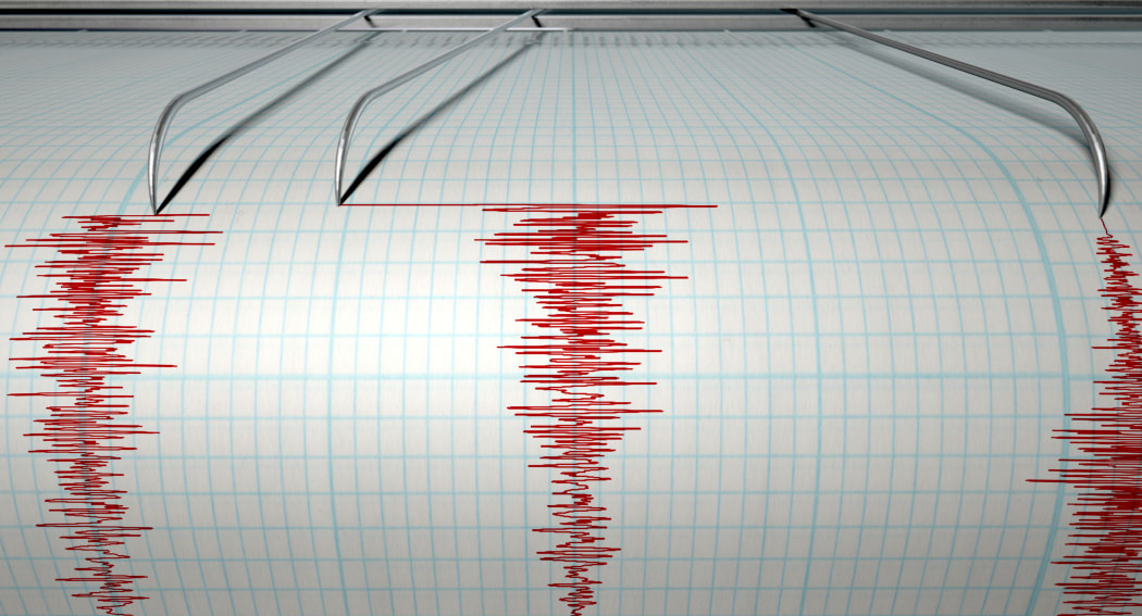 A closeup of a seismograph machine needle drawing a red line on graph paper depicting seismic and eartquake activity on an isolated white background