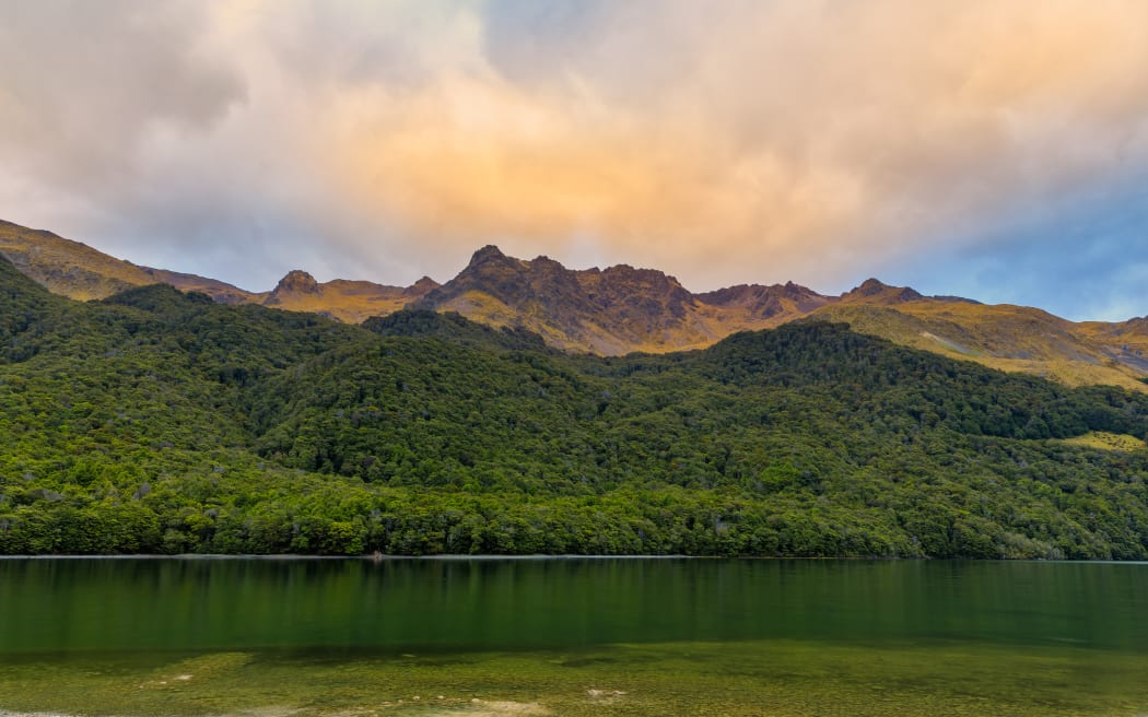 Forests and mountains surrounding North Mavora Lake at sunset on a cloudy day.