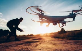 Drone trends and innovations. Modern hobby and leisure. Closeup of camera quadcopter controlled remotely by guy over blur sunset.