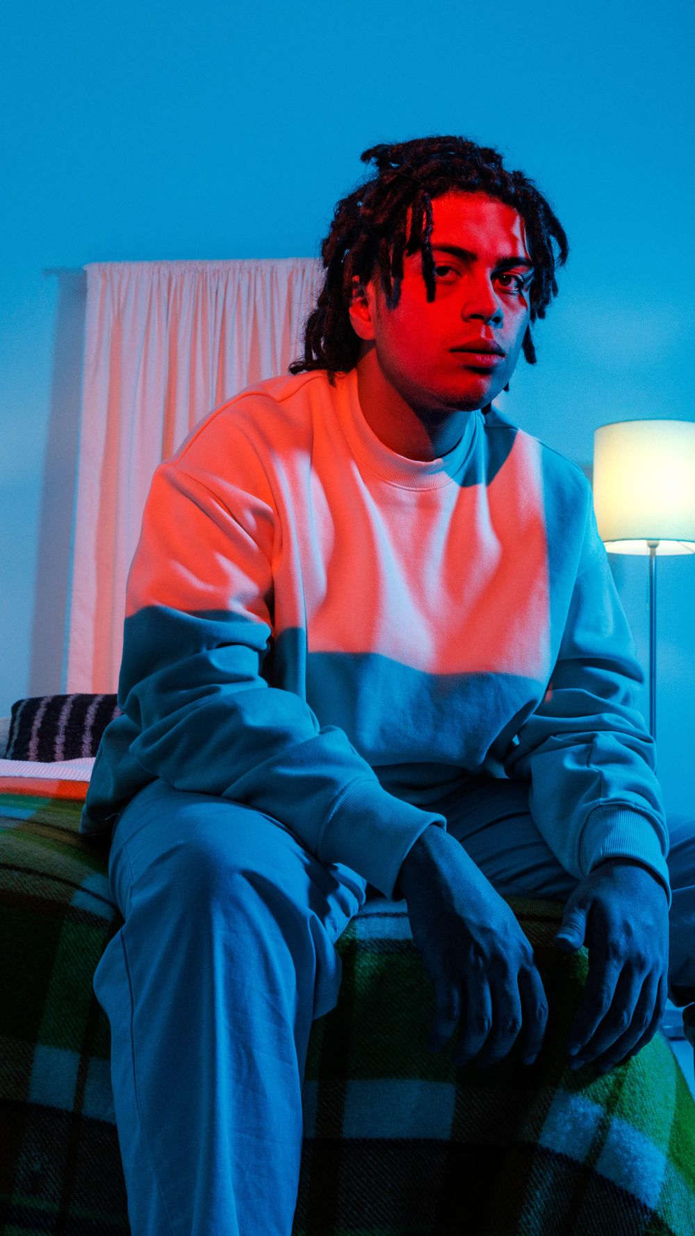 Denzel sitting at the end of a bed in a fluorescent blue and red room
