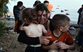 A Syrian woman holds her children as they arrive on an overcrowded dinghy on a beach near the port on the Greek island of Kos on 15 August.