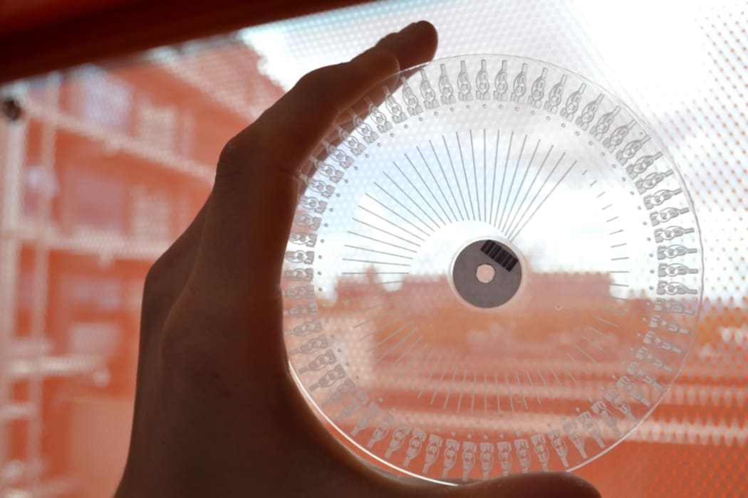 An example of a transparent disc, with carved channels and wells visible, used to analyse milk samples.