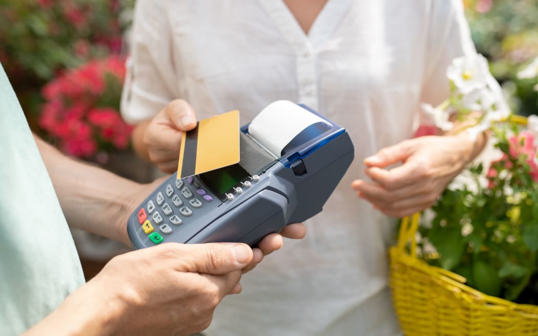 Pembeli wanita kontemporer menggunakan kartu kredit untuk membayar beberapa pot bunga segar di pusat taman kontemporer