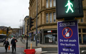 Pedestrians pass a sign displaying a COVID-19 sign advising pedestrians not to use the button, is displayed on a traffic light pole in the centre of Bradford, west Yorkshire on October 31, 2020, as the number of cases of the novel coronavirus COVID-19 rises.