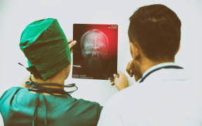 Doctor and surgeon examining x-ray film of patient's head for brain, skull or eye injury.
