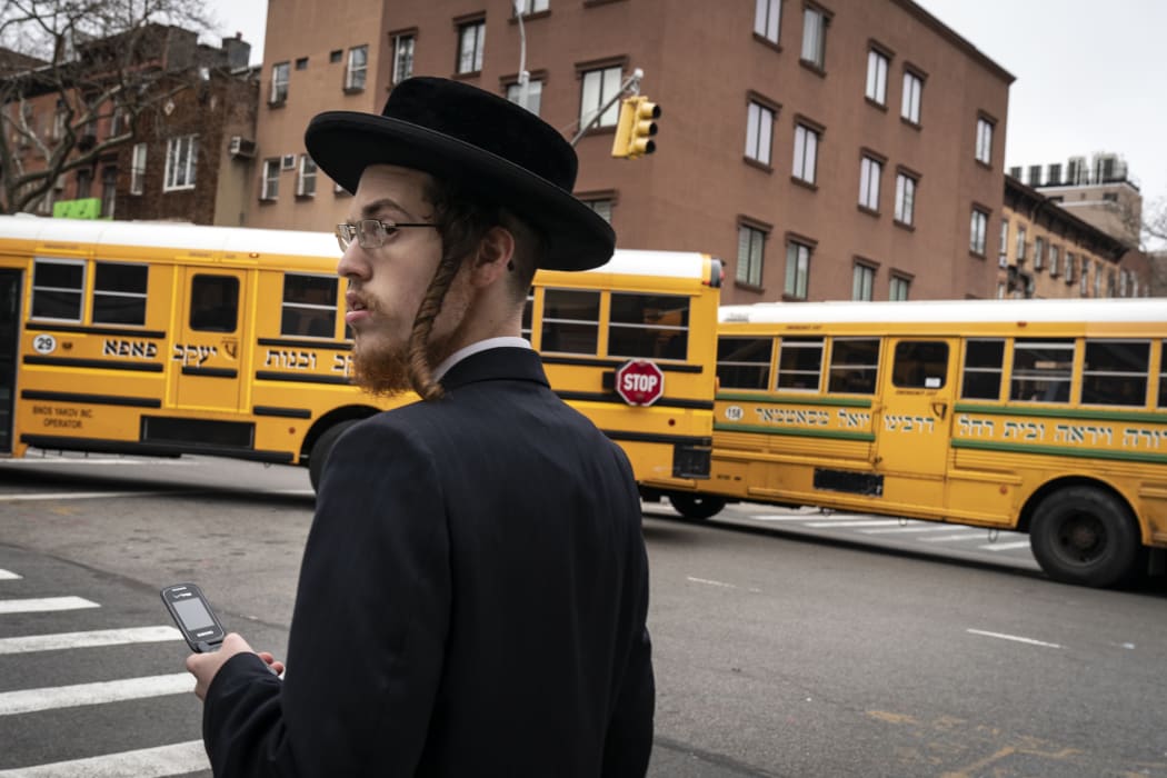 A man walks past school buses in a South Williamsburg neighborhood. A public health emergency has been declared in the  area.
